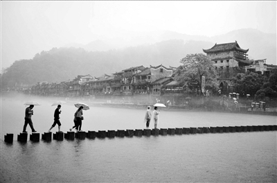 4月29日，游客冒雨走过沱江上的跳岩。新华社发