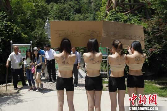 四女子仅着贴身衣物举牌邀游客在其身体上签名“到此一游”。 曹铮铮 摄
