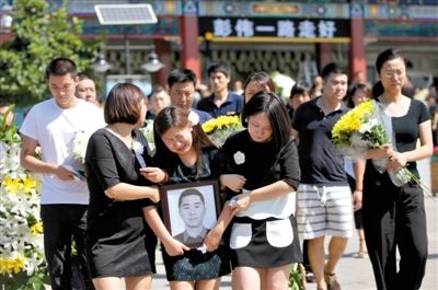 昨日，八宝山殡仪馆，杨璐在亲友搀扶下捧着丈夫彭伟的遗像参加追悼会。8月9日，因喷泉漏电，彭伟为救两只爱犬遭触电身亡。新京报记者 薛珺 摄