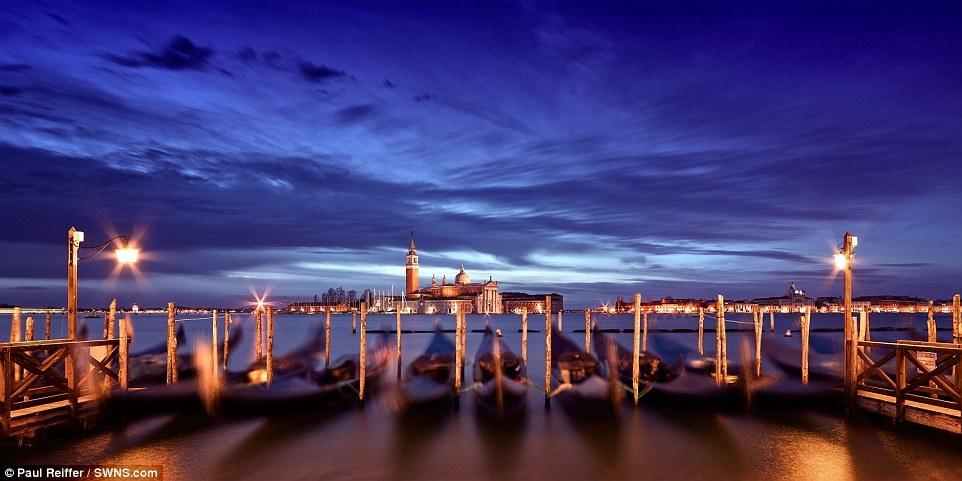 【意大利威尼斯、黎明】这张照片是Reiffer搭乘前往圣马可广场的水上巴士时拍摄的。一排贡多拉（威尼斯平底船）静静地停靠在港口随着河水起起伏伏，远处的古堡被在深蓝色的云层下显得格外静谧。