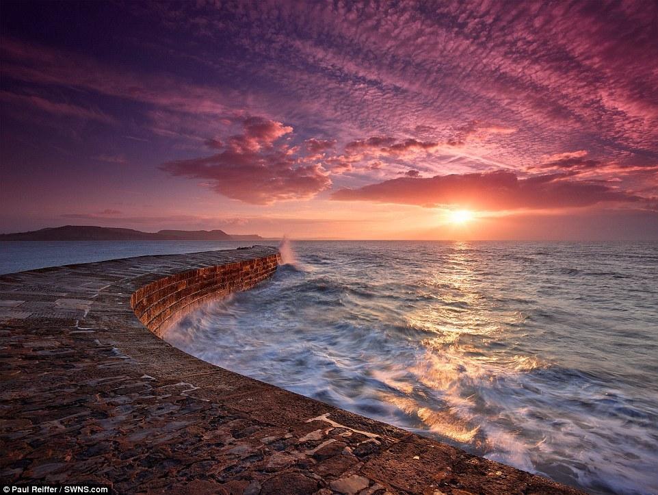 【英国莱姆里杰斯科布河、日出】波涛汹涌的海面使这张照片看起来充满动感。浪花在科布河古老的港口墙上来回拍打，日出的光芒洒落在这座英国海滨小城上。